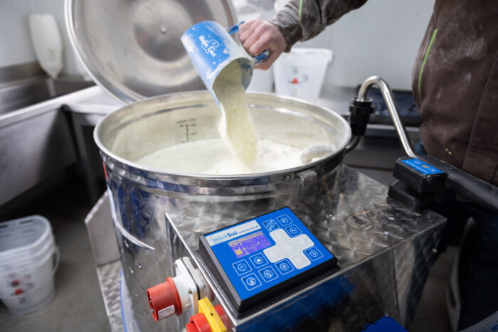 This photo shows a scoop of milk replacer powder being added to an already filled MilkTaxi.