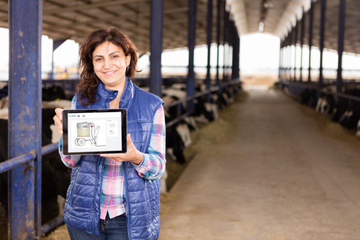 In questa immagine una donna tiene in mano un tablet, sul quale si può vedere la connessione a CalfGuide taxi del latte. La donna è nel recinto dei vitelli.