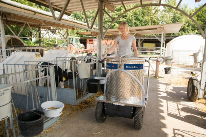 This picture shows a farmer with a MilkTaxi in a CalfGarden. She is dispensing milk into a feeding bucket.