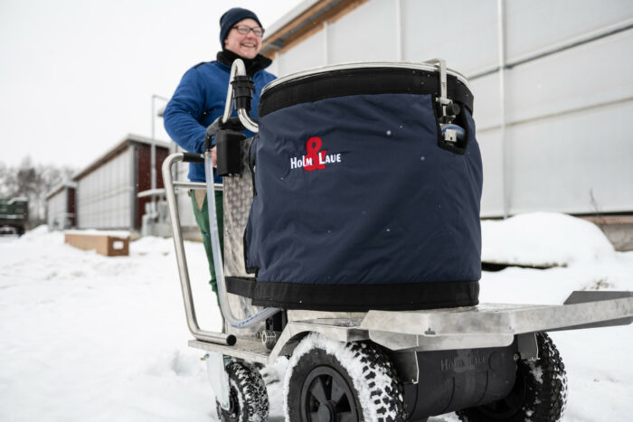 This photo shows a MilkTaxi with jacket. It is being pushed through the snow by a female farmer.